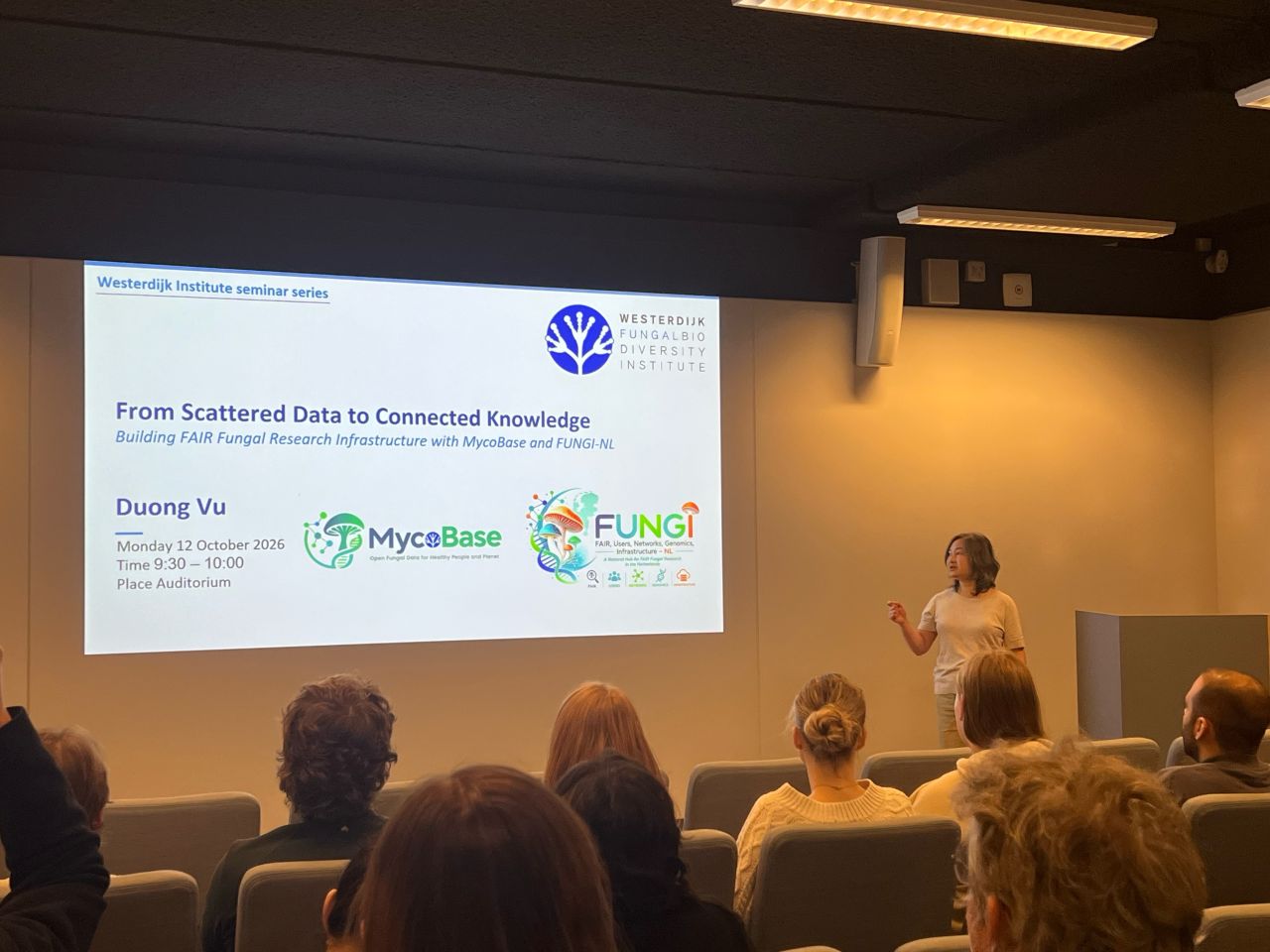 Duong Vu presenting MycoBase and FUNGI-NL at the Westerdijk Institute seminar series on 12 October 2026, standing next to a projected title slide that shows the MycoBase and FUNGI-NL logos.